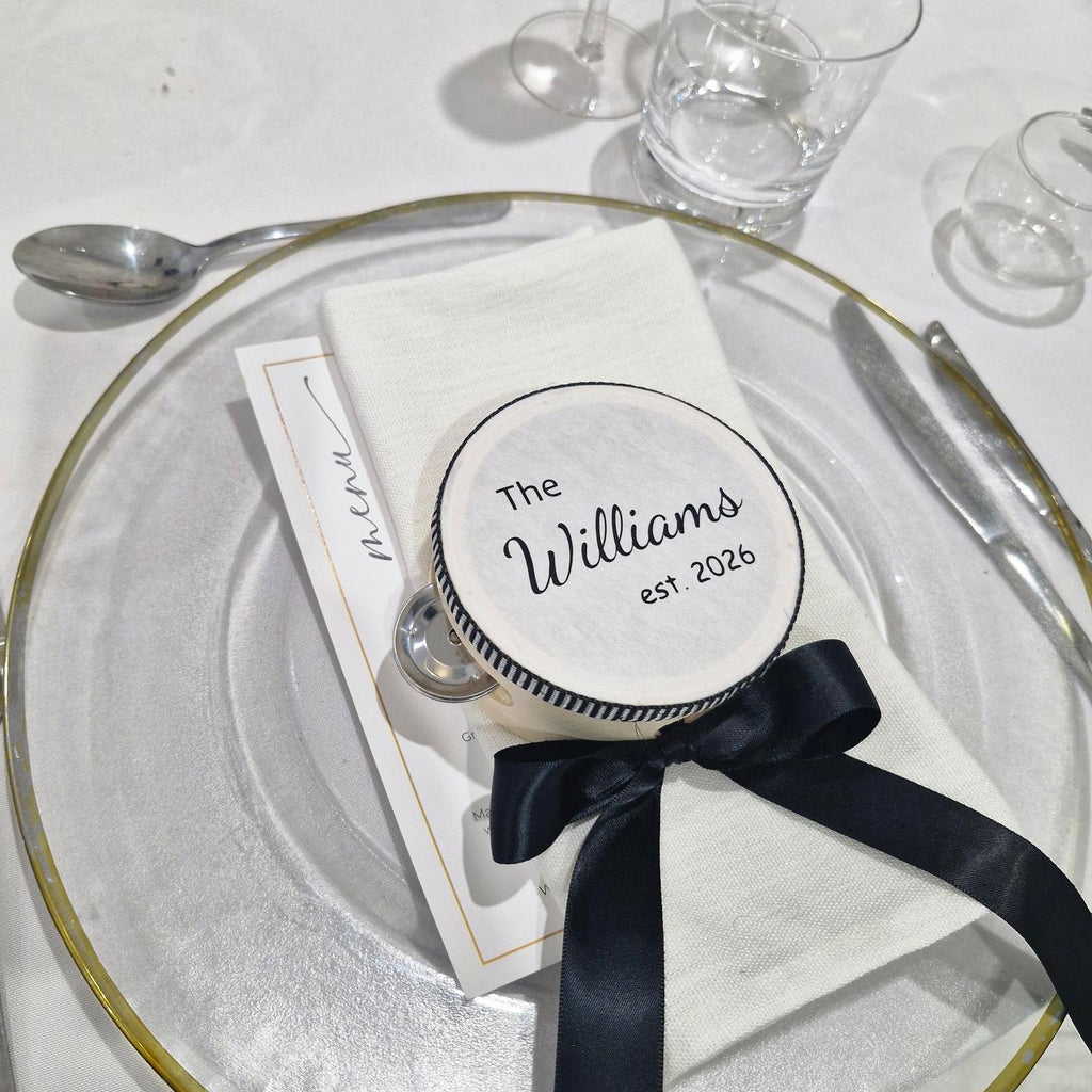 Personalized wedding favour tambourine with a black ribbon on a glass plate with glasses in the background.