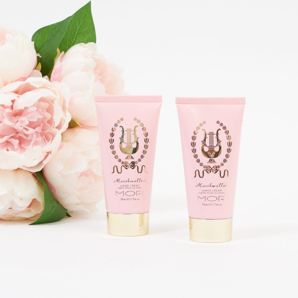 Two pink tubes of MOR hand cream product with flowers on a white background