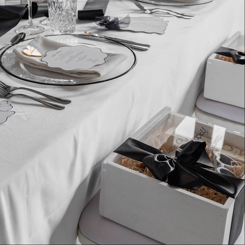 Elegant table setting with white tablecloth, silverware, and candles in a formal setting with a white gift box on the seat.