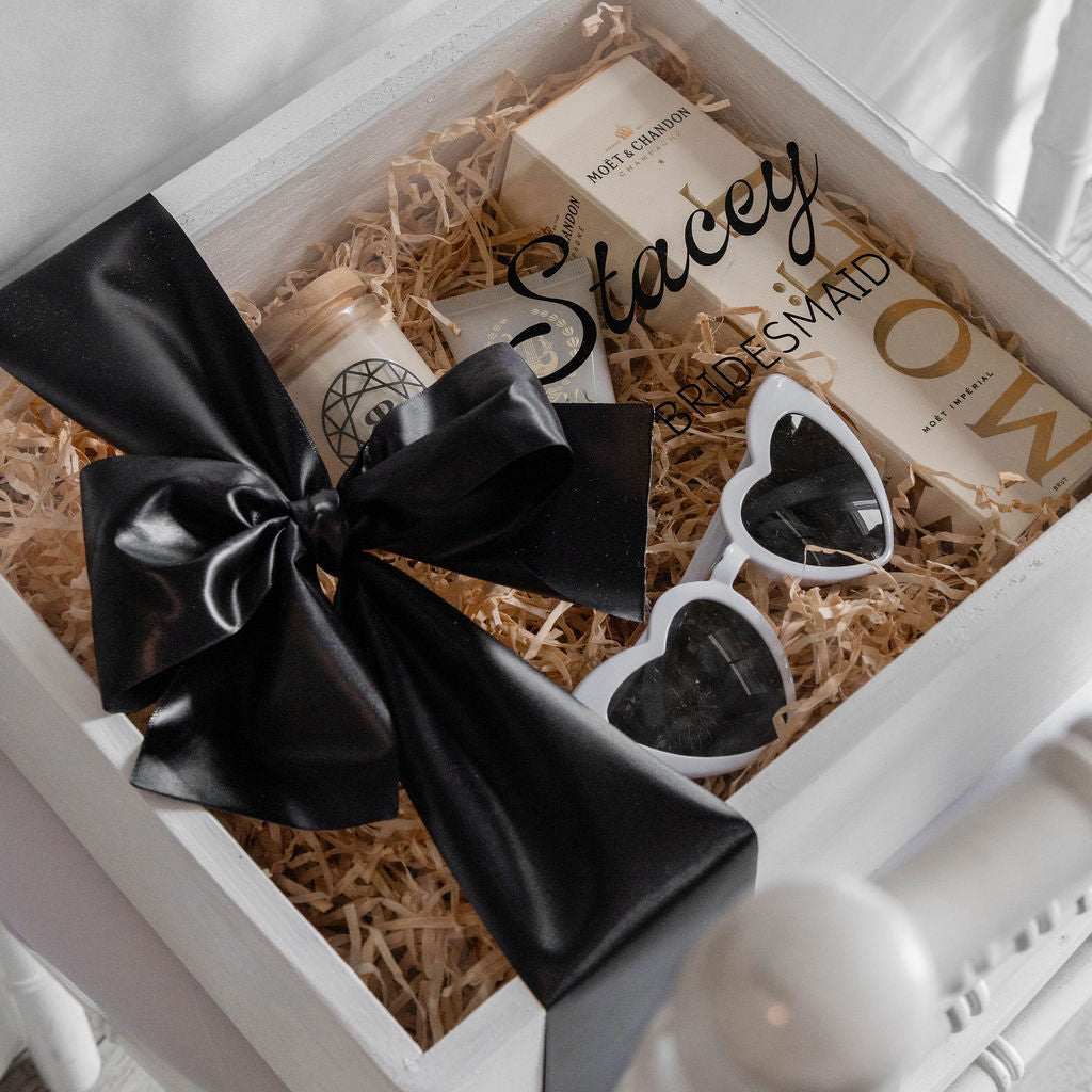 Gift box with black bow, heart-shaped sunglasses, and branded items on a white background