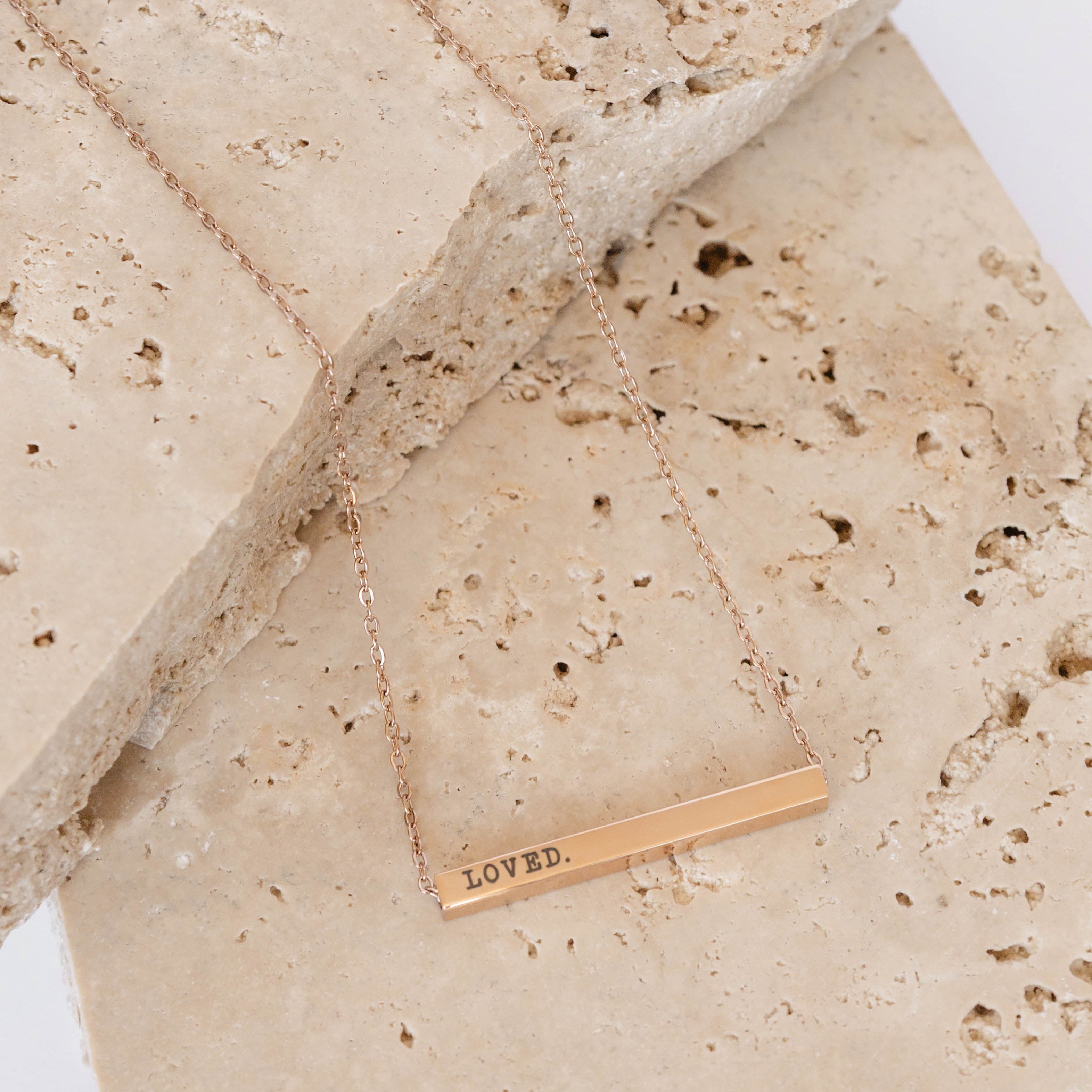 Gold necklace with 'LOVED' pendant on a textured beige surface