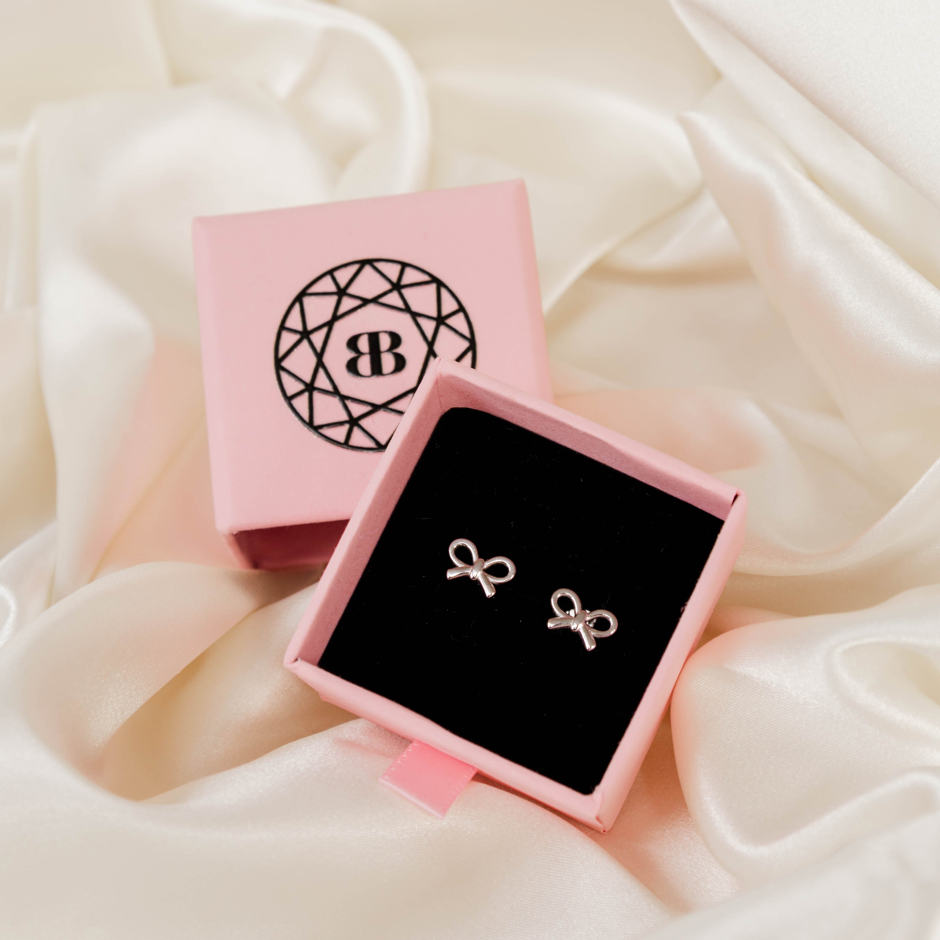 Silver bow earrings in a pink jewellery box on a soft fabric background
