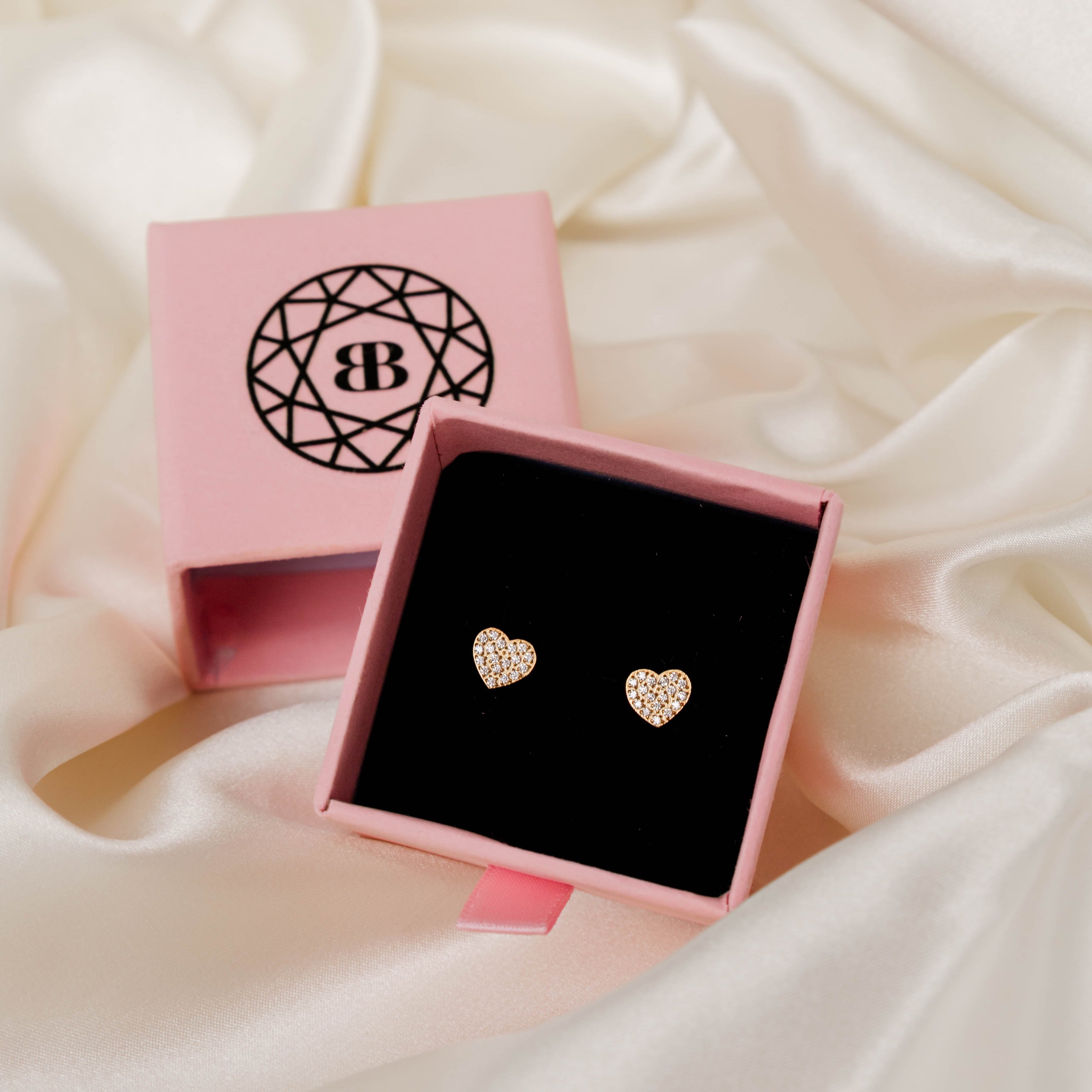 Heart-shaped earrings in a pink box on a soft fabric background