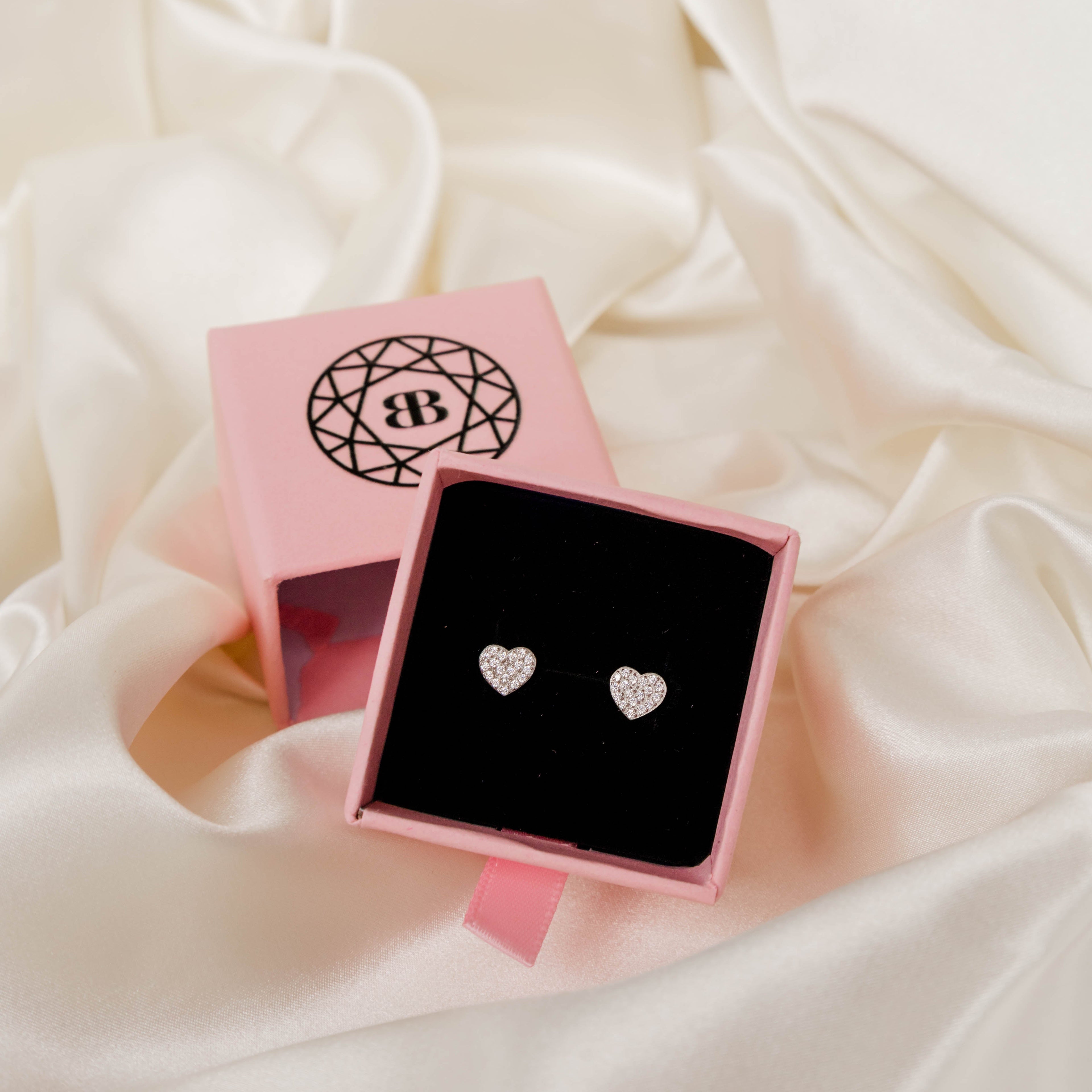 Heart-shaped earrings in a pink jewellery box on a soft fabric background