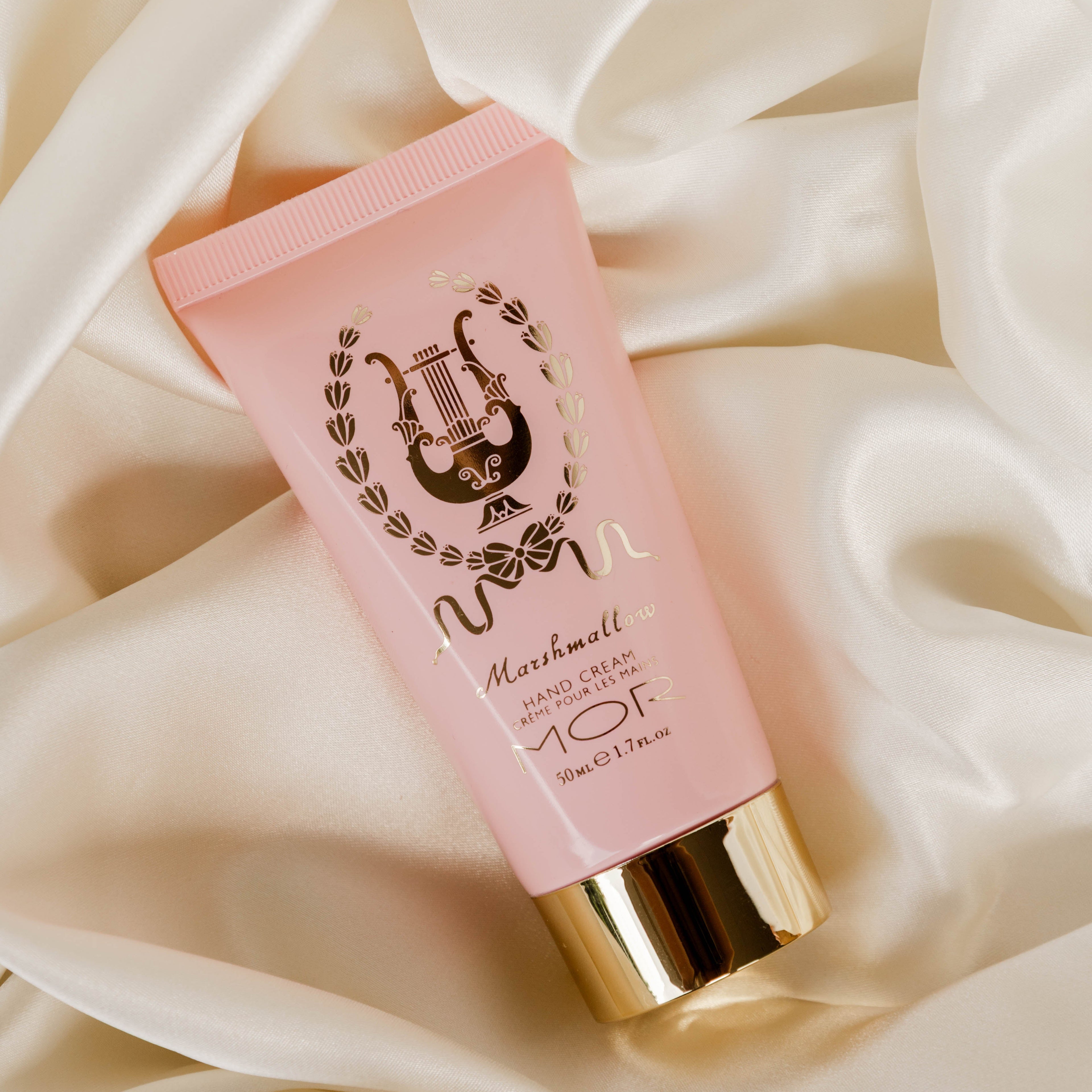 Pink tube of hand cream with gold cap on a soft beige fabric background