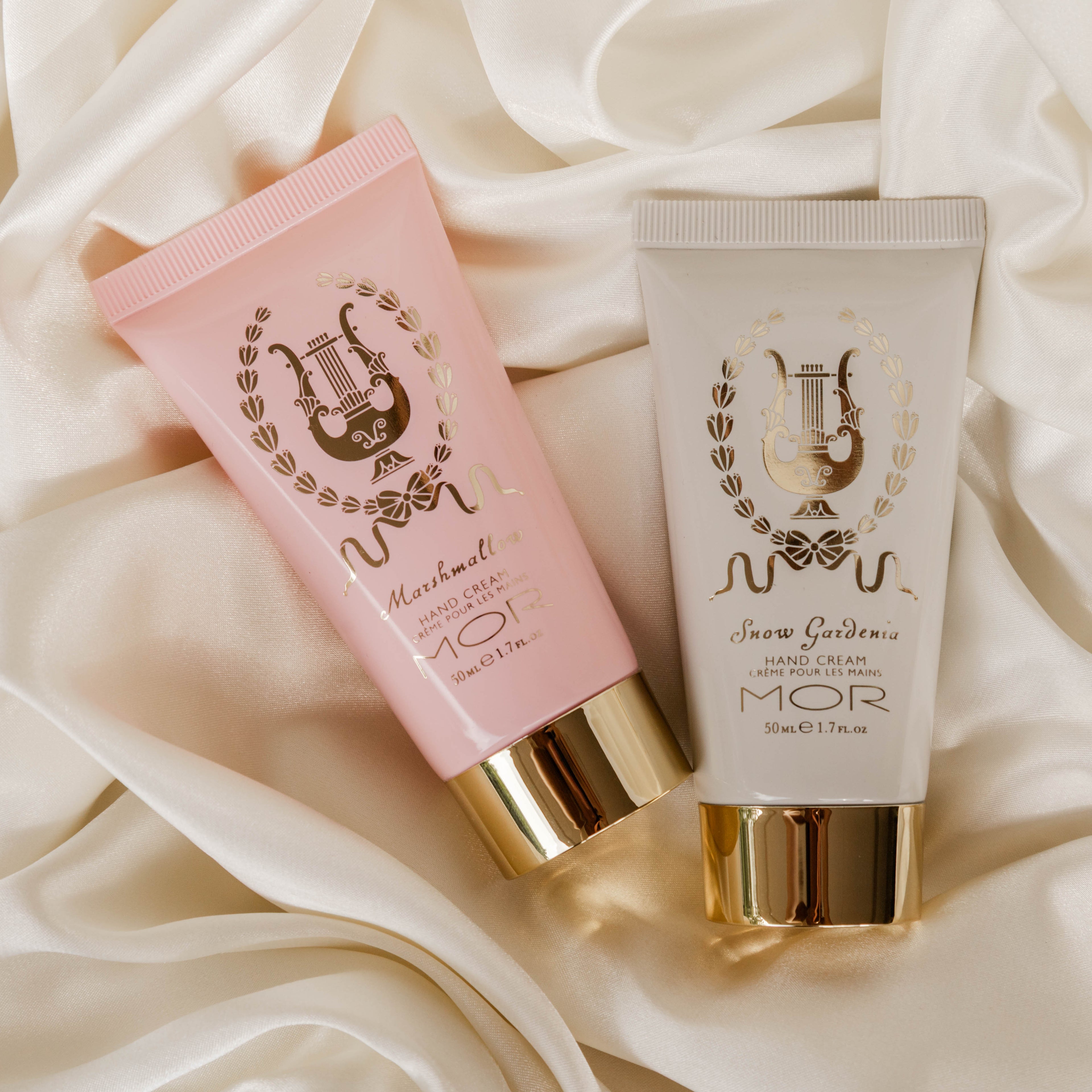 Two cosmetic tubes of hand cream with gold accents on a soft fabric background