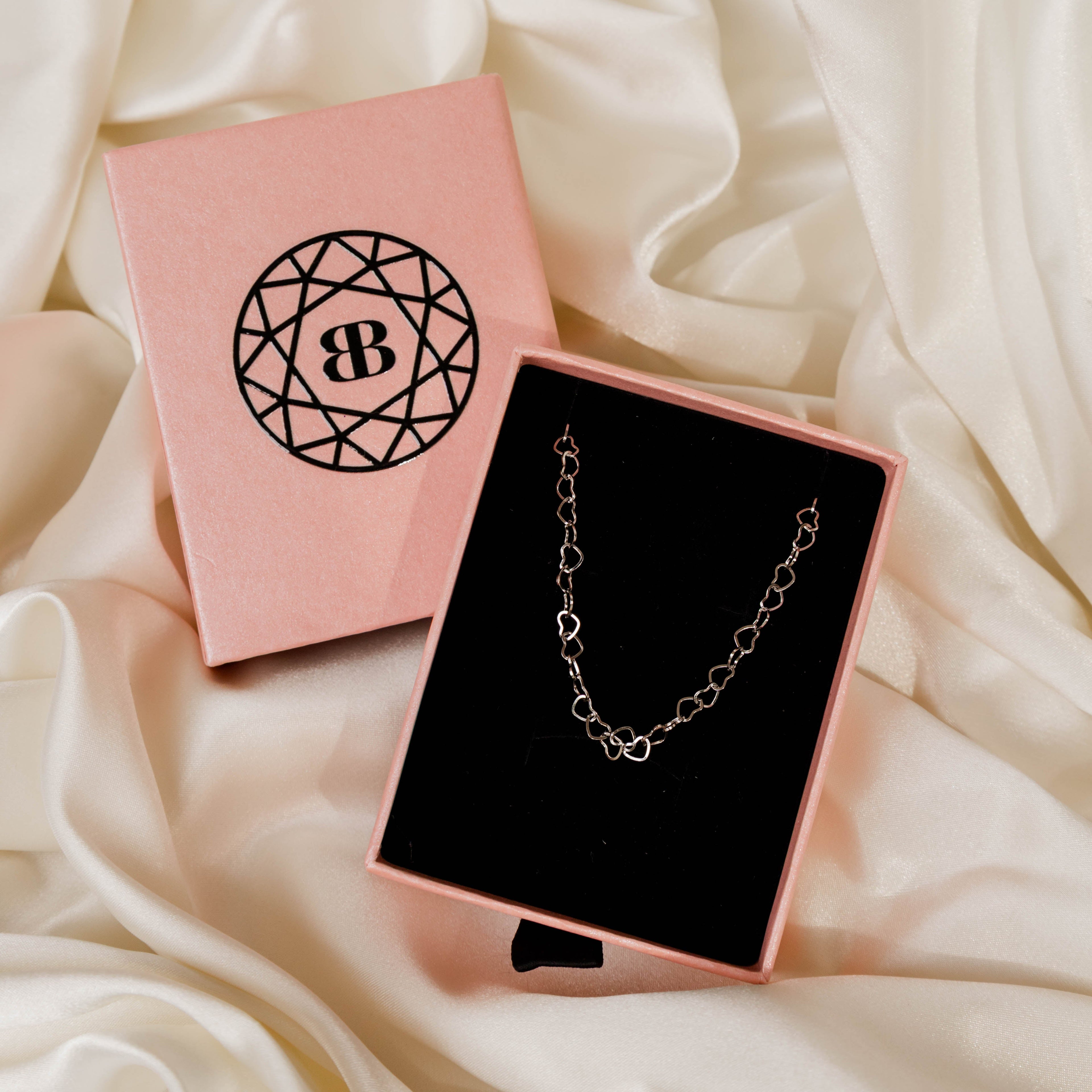 Silver bracelet in a pink jewellery box with a brand logo on a white fabric background