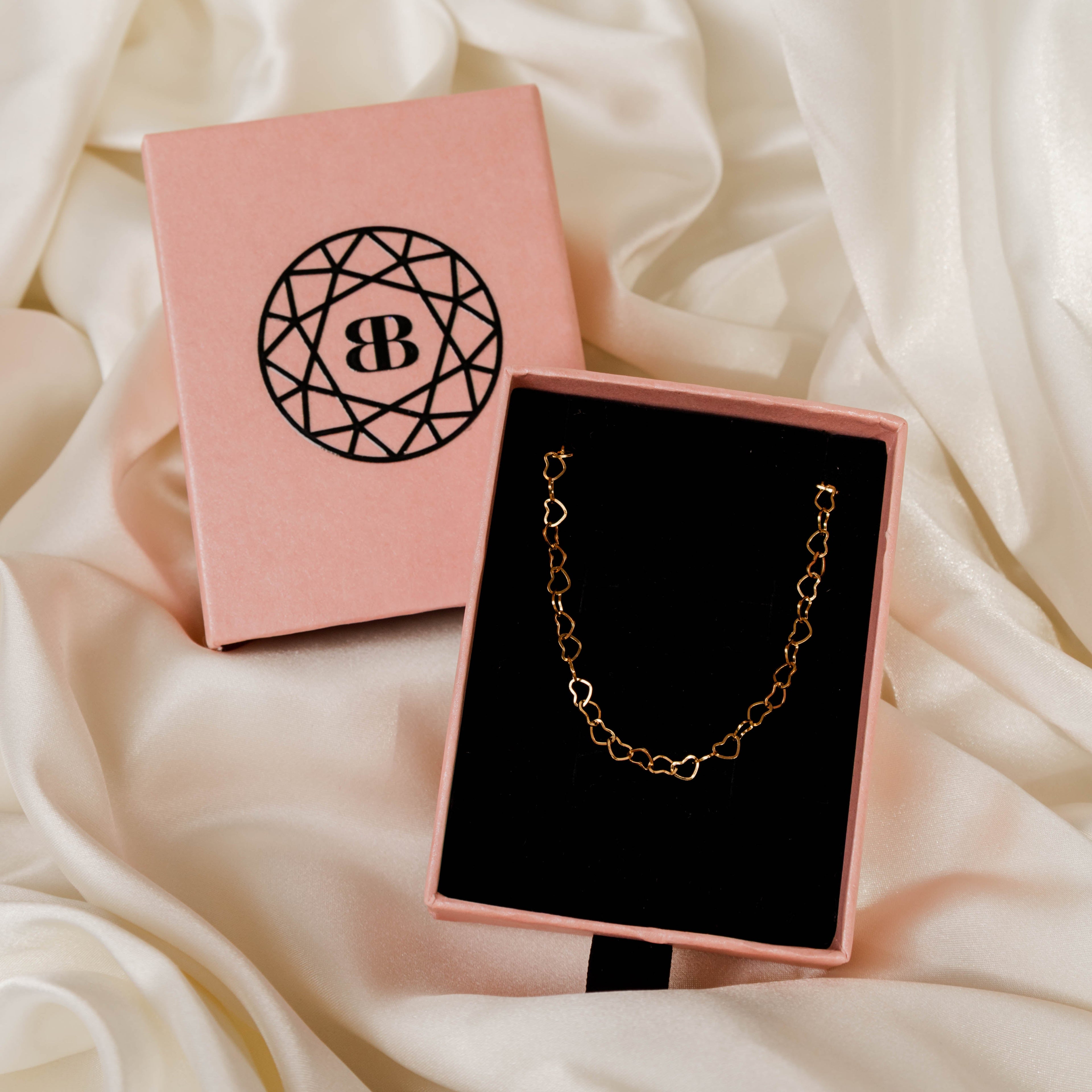 Gold chain bracelet in a pink jewellery box with a visible brand logo on a white fabric background