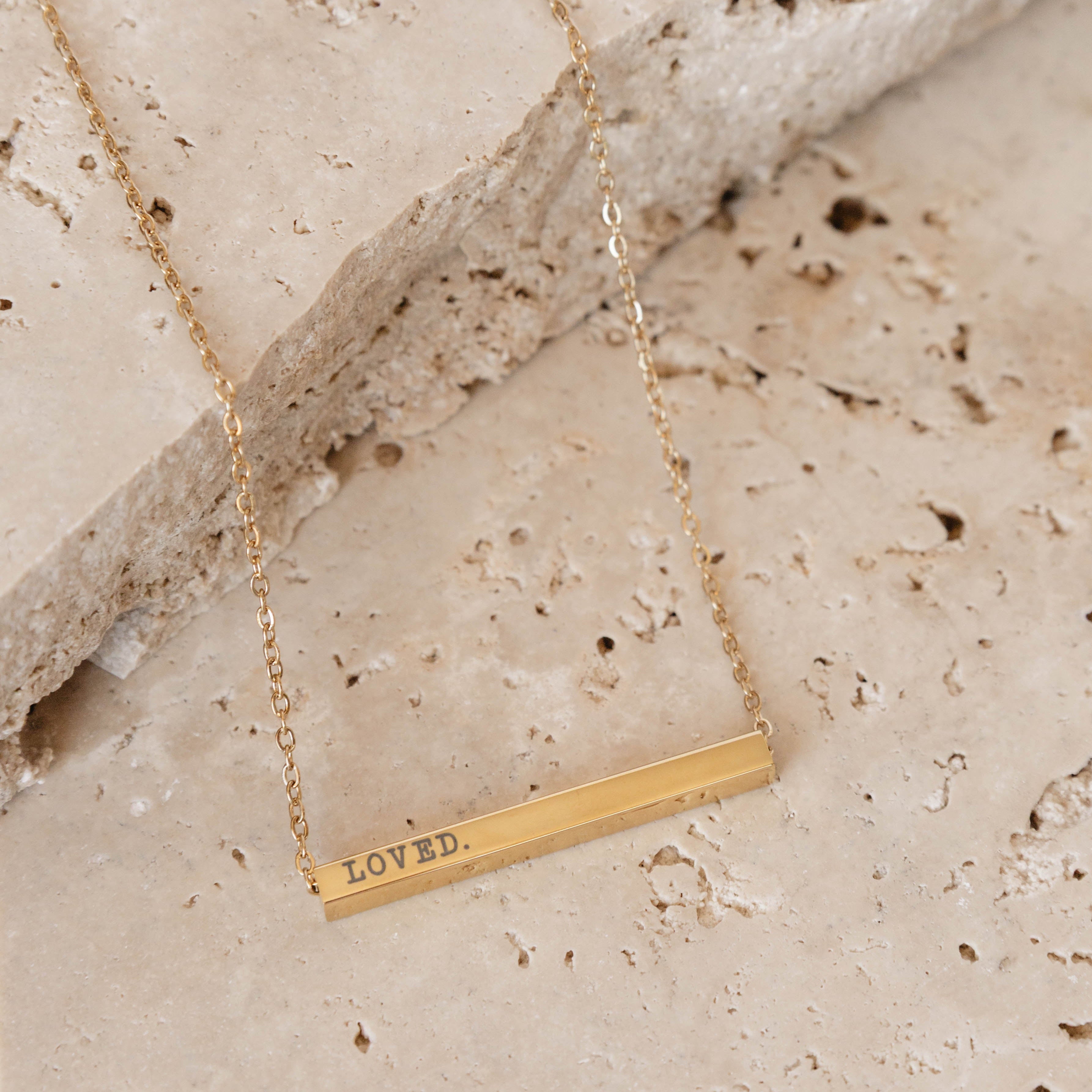 Gold necklace with 'LOVED' pendant on a stone surface