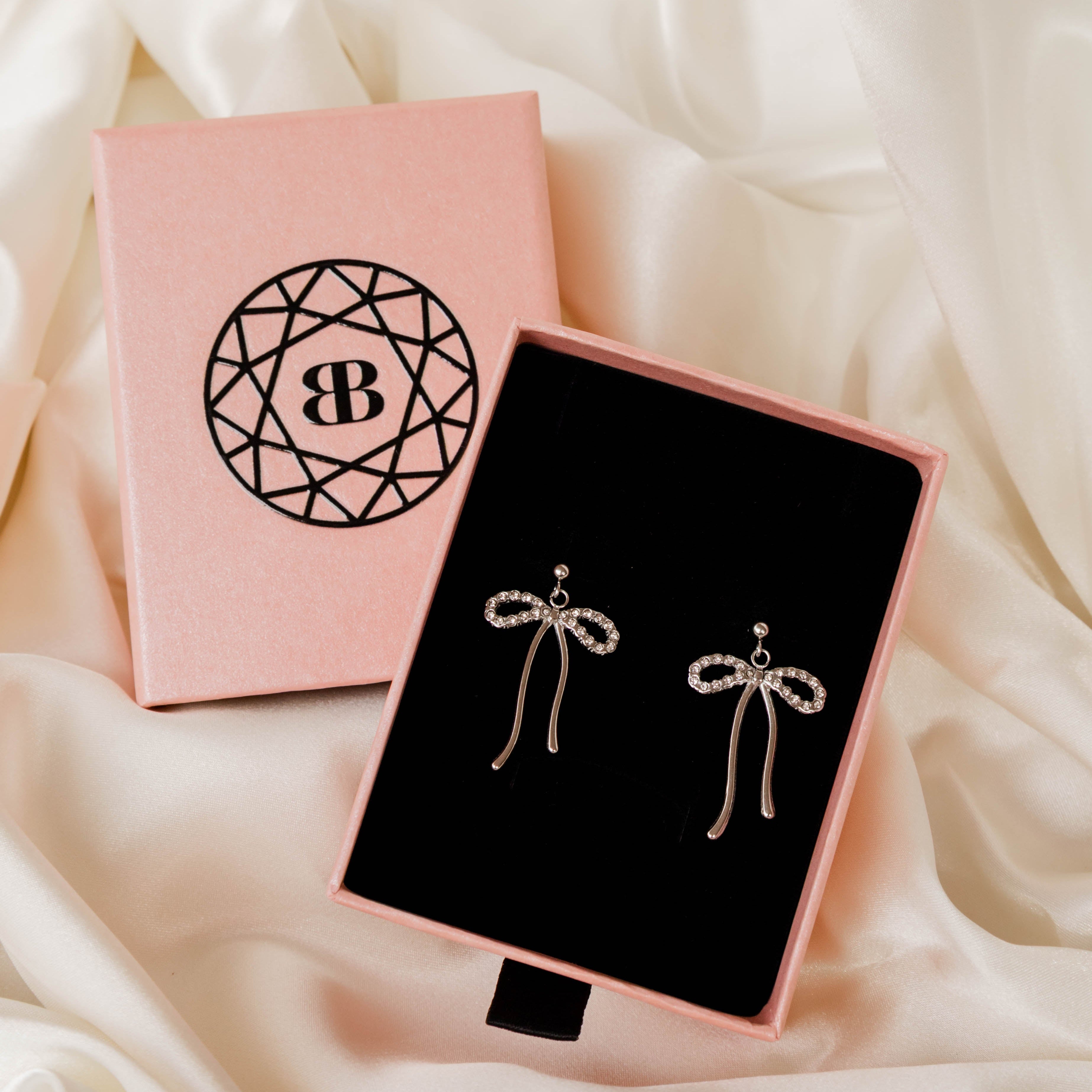 Bow-shaped earrings in a pink and black box on a soft white fabric background