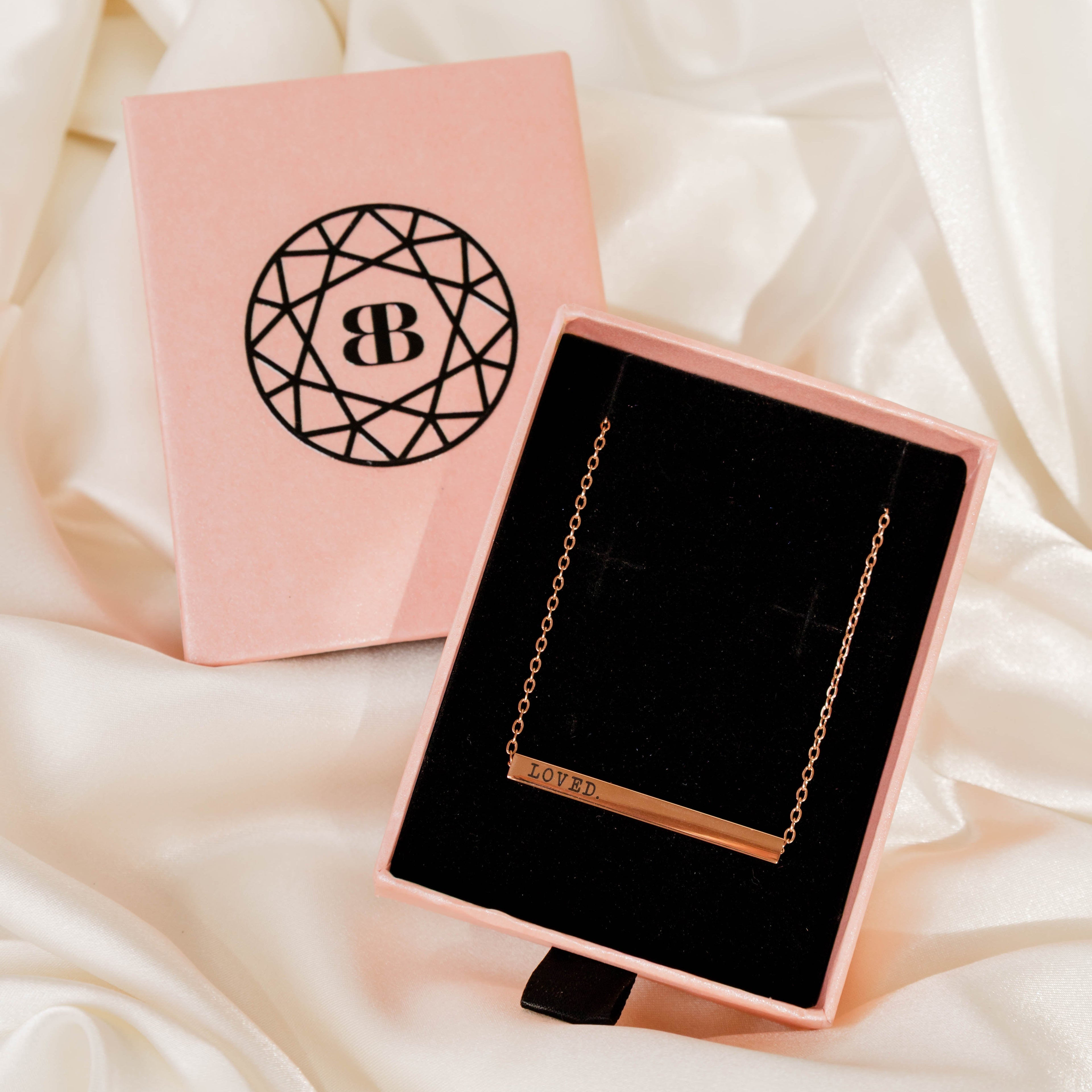 Necklace in a pink box with a visible brand logo on a soft white fabric background