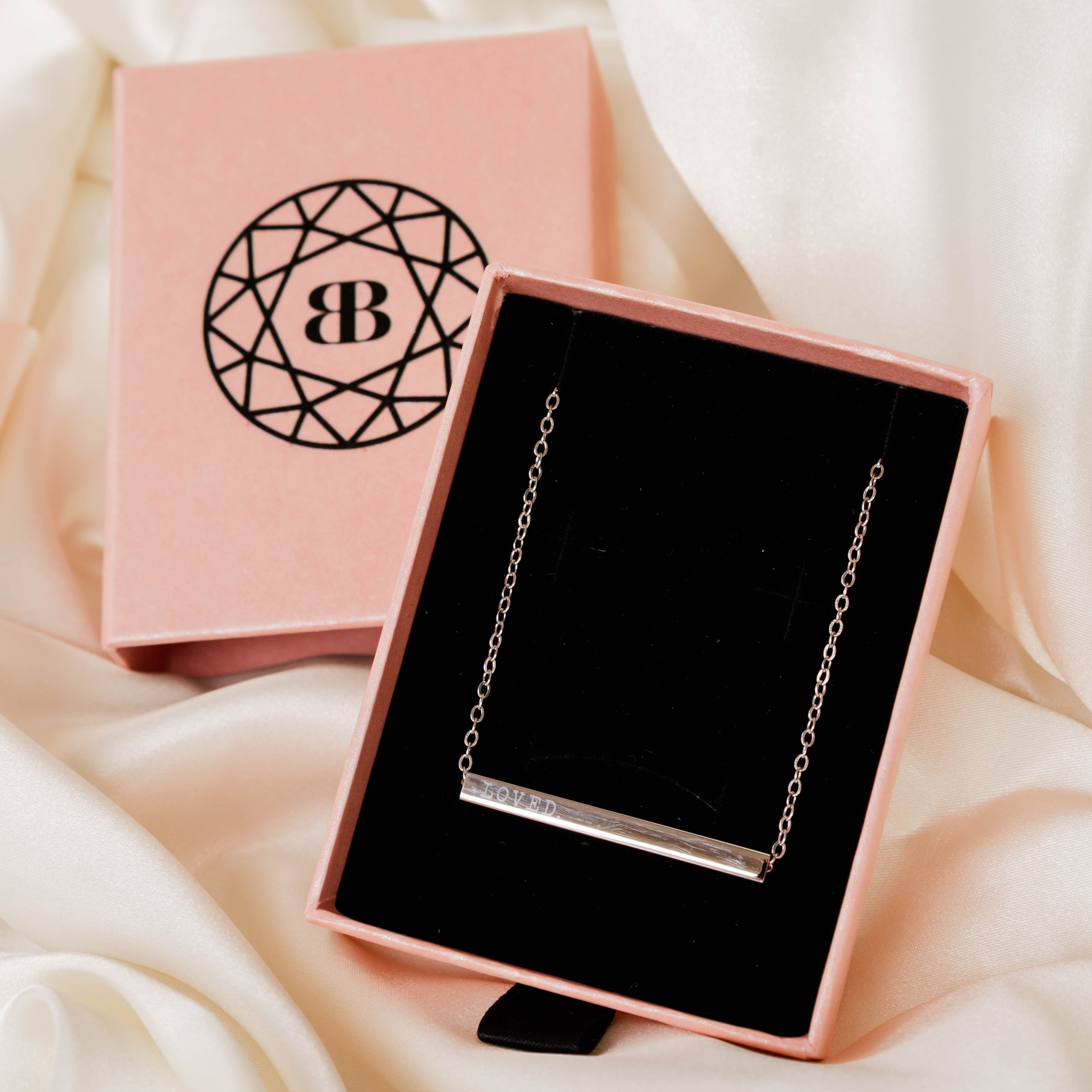 Gold necklace in a pink jewelry box with a visible brand logo on a soft white fabric background