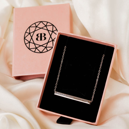 Gold necklace in a pink jewelry box with a visible brand logo on a soft white fabric background