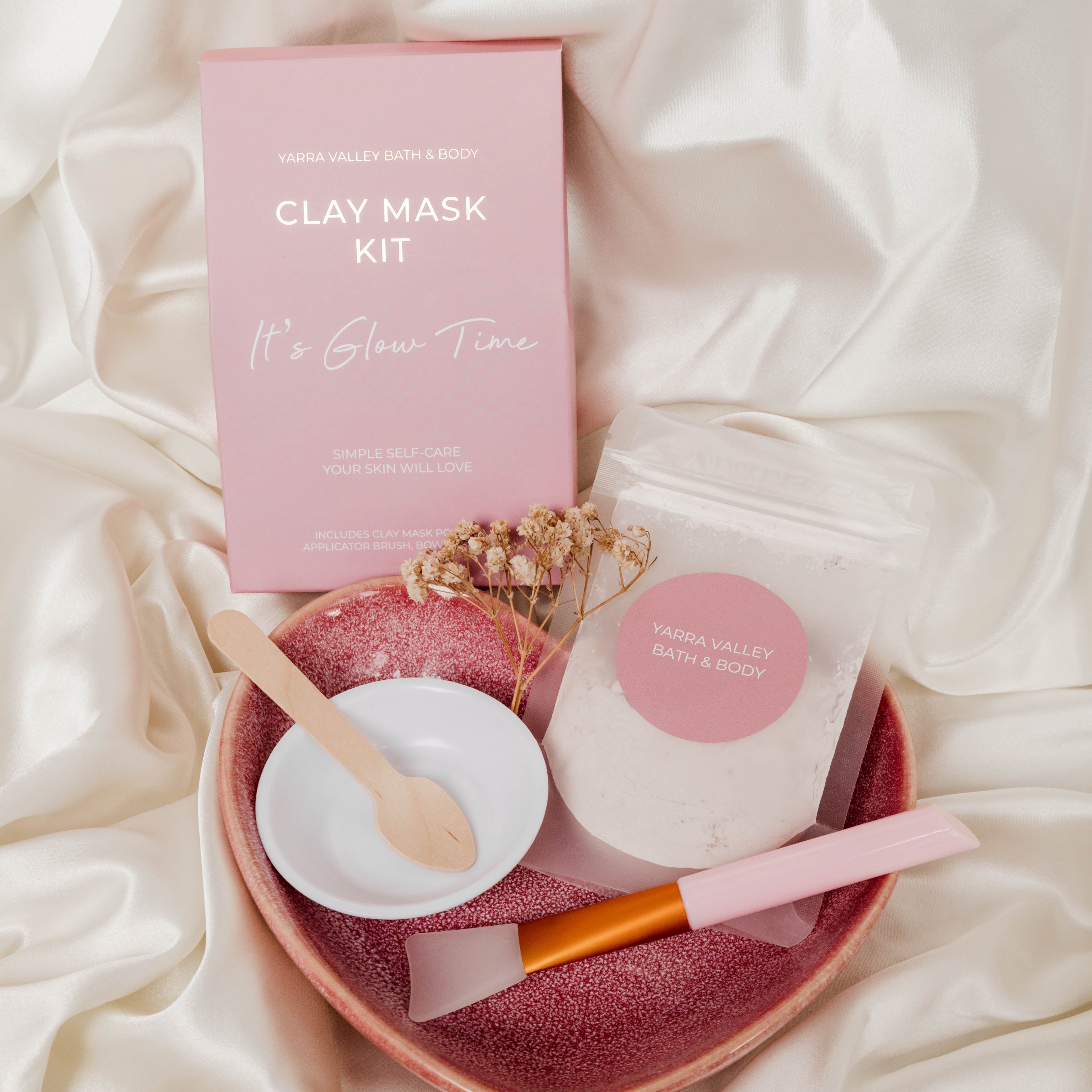Clay mask kit with pink packaging, white mask, brush, and bowl on a soft fabric background