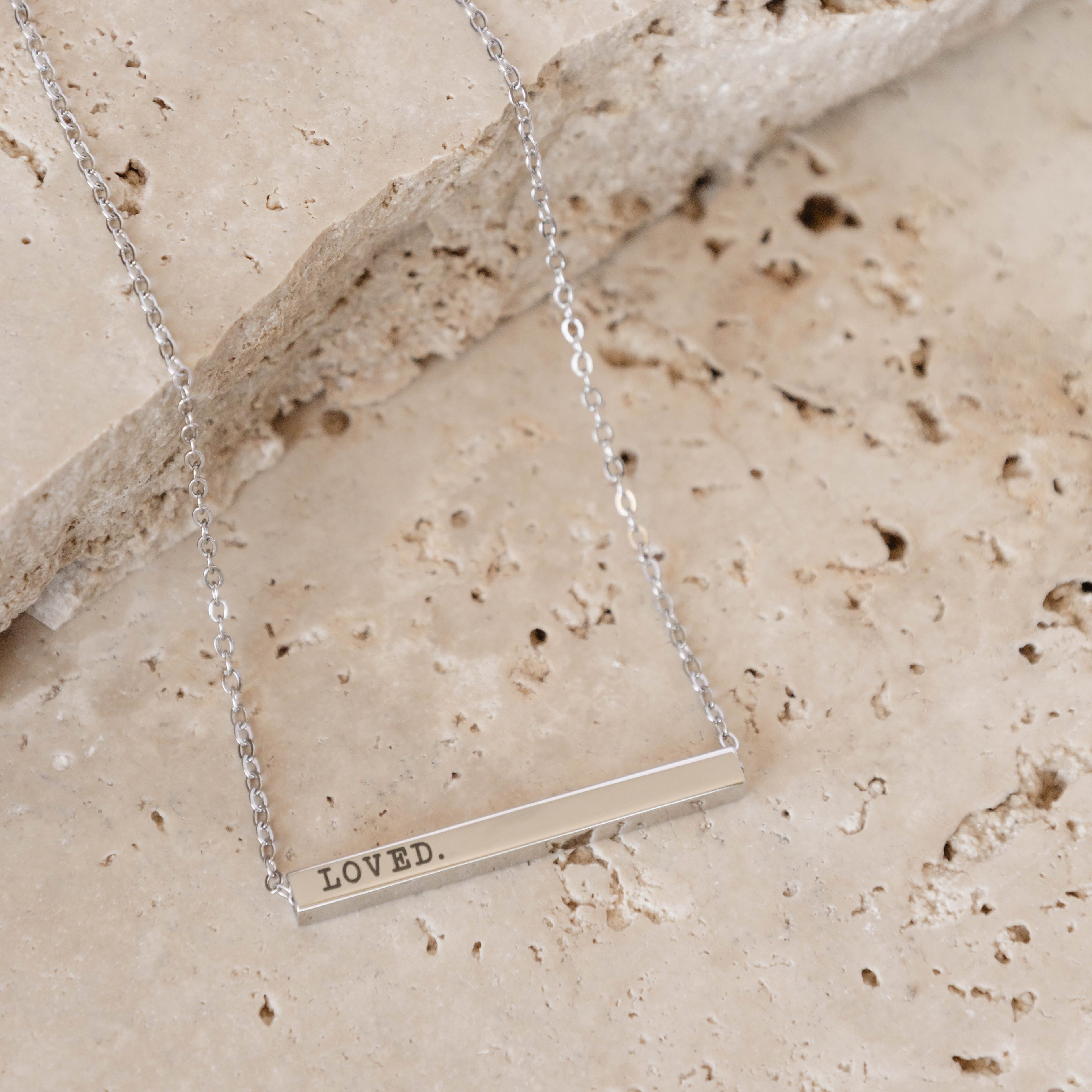 Silver necklace with a 'LOVED' pendant on a stone surface