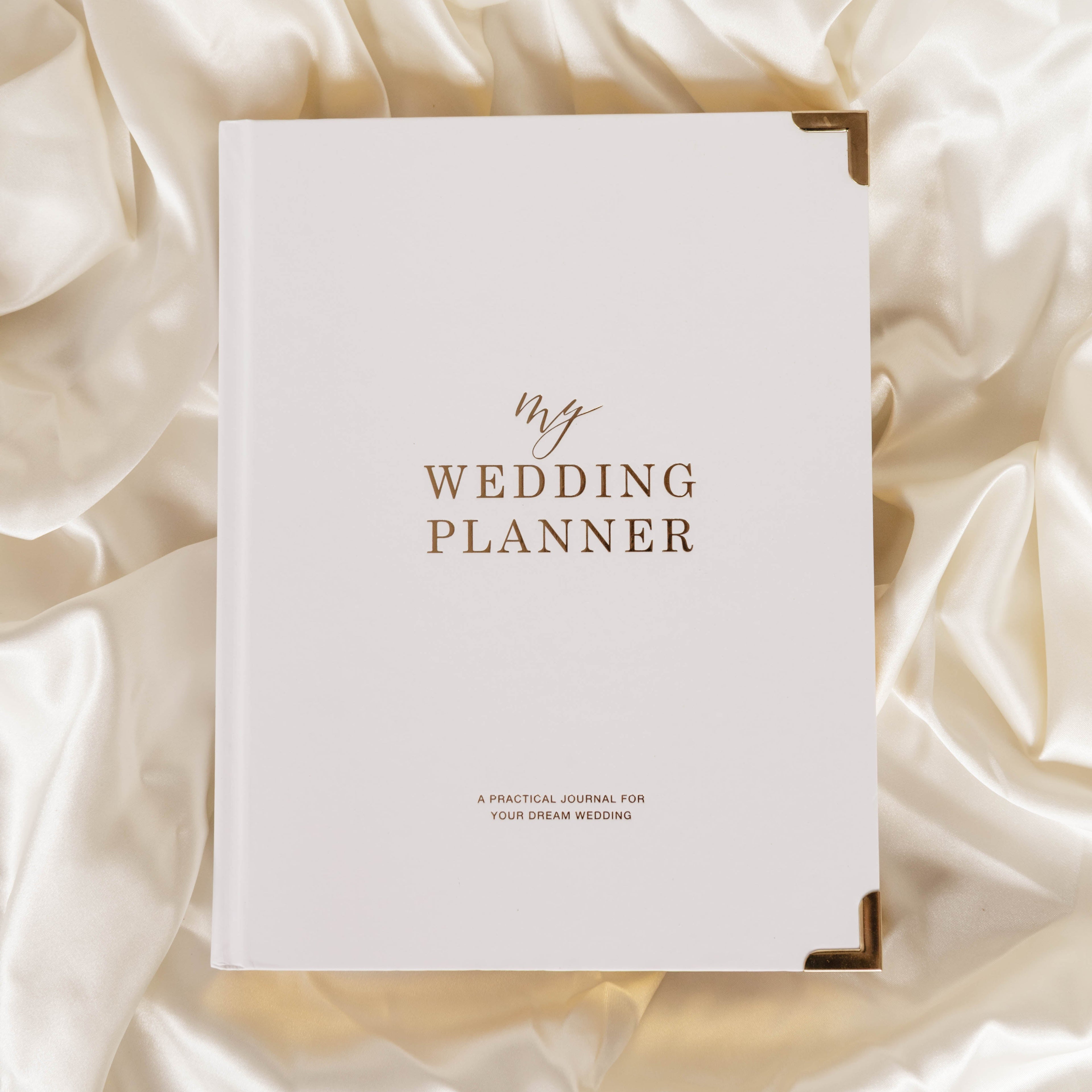 White wedding planner book with gold text on a soft, light-colored fabric background