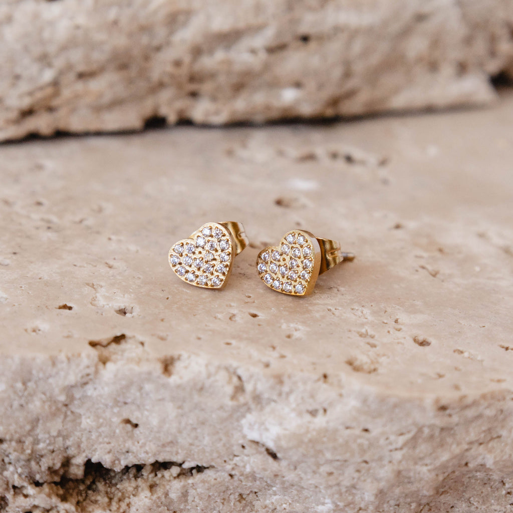 Heart-shaped gold earrings with clear stones on a textured stone surface