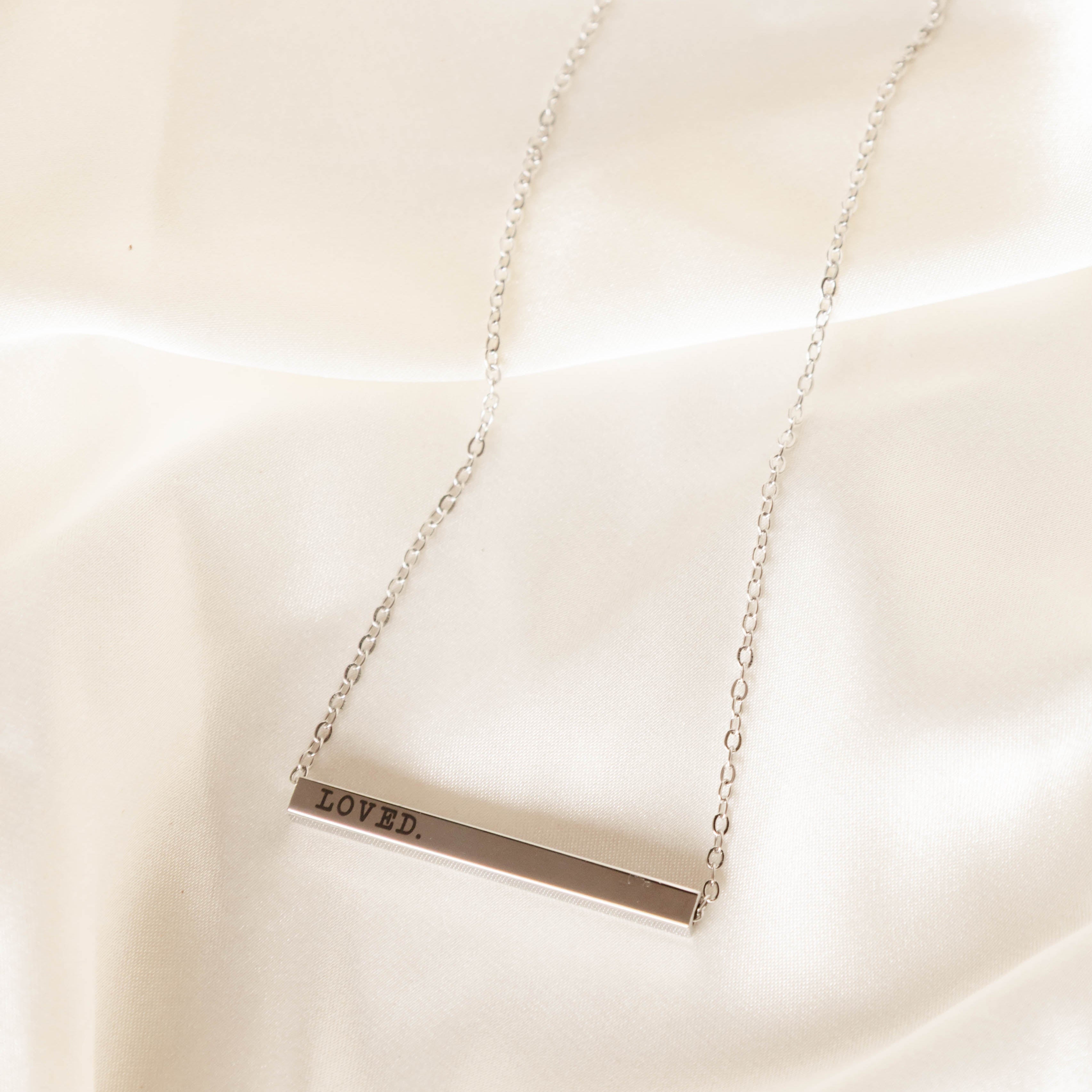 Silver necklace with a rectangular pendant on a white fabric background