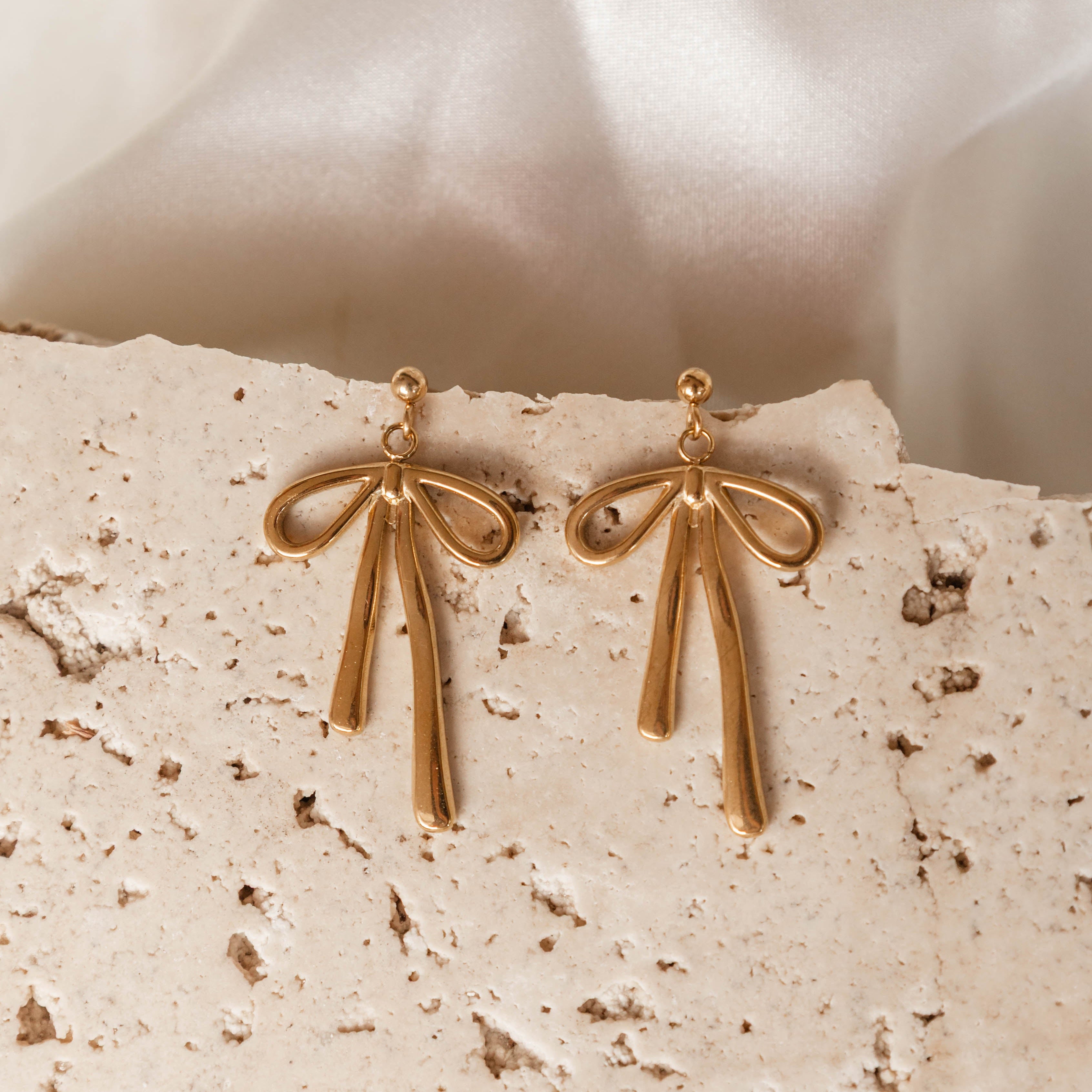 Gold bow-shaped earrings on a textured beige surface