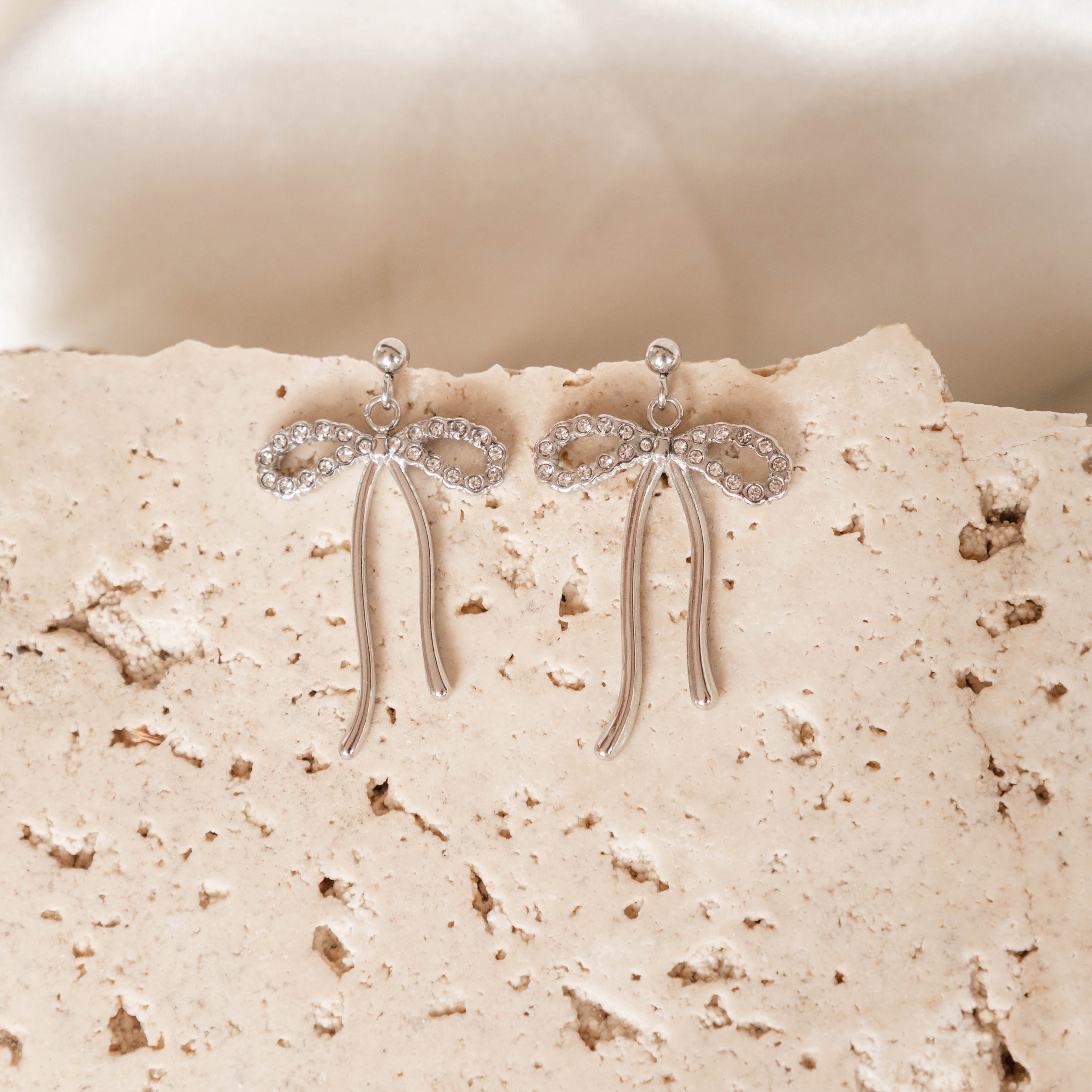 Silver earrings with bow design on a textured beige surface