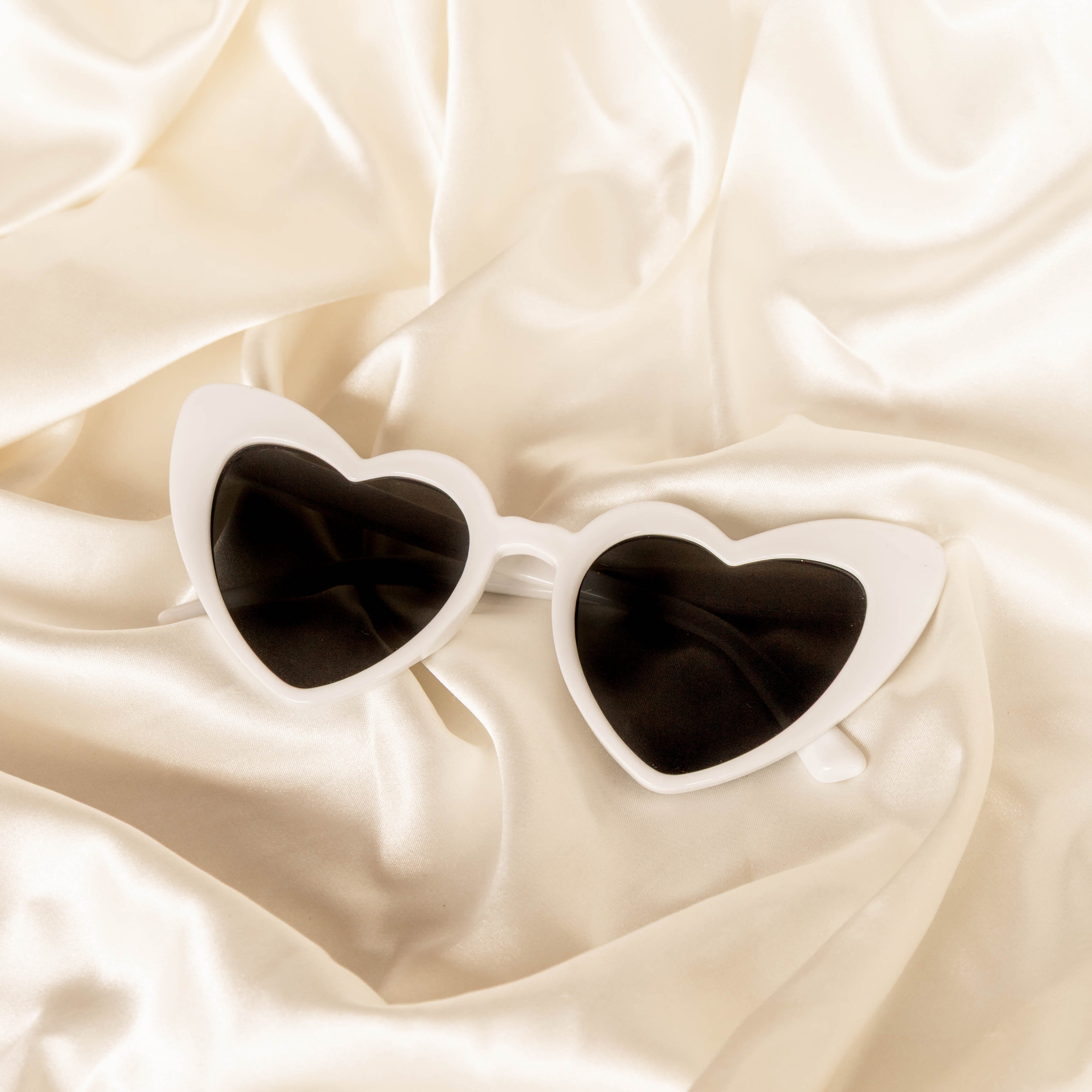 Heart-shaped sunglasses on a beige satin background