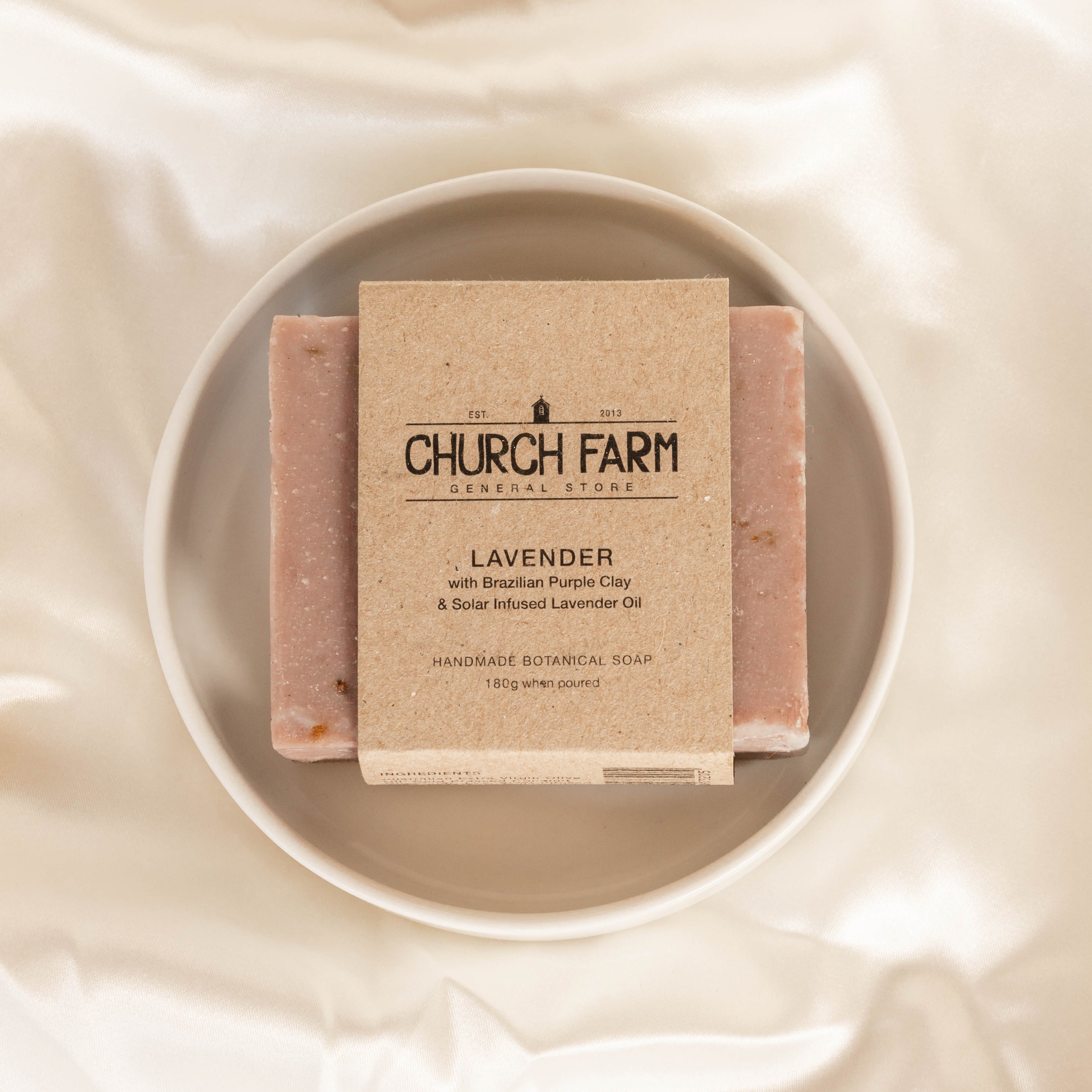 Bar of soap with a 'Church Farm' label on a white plate, set against a beige fabric background.