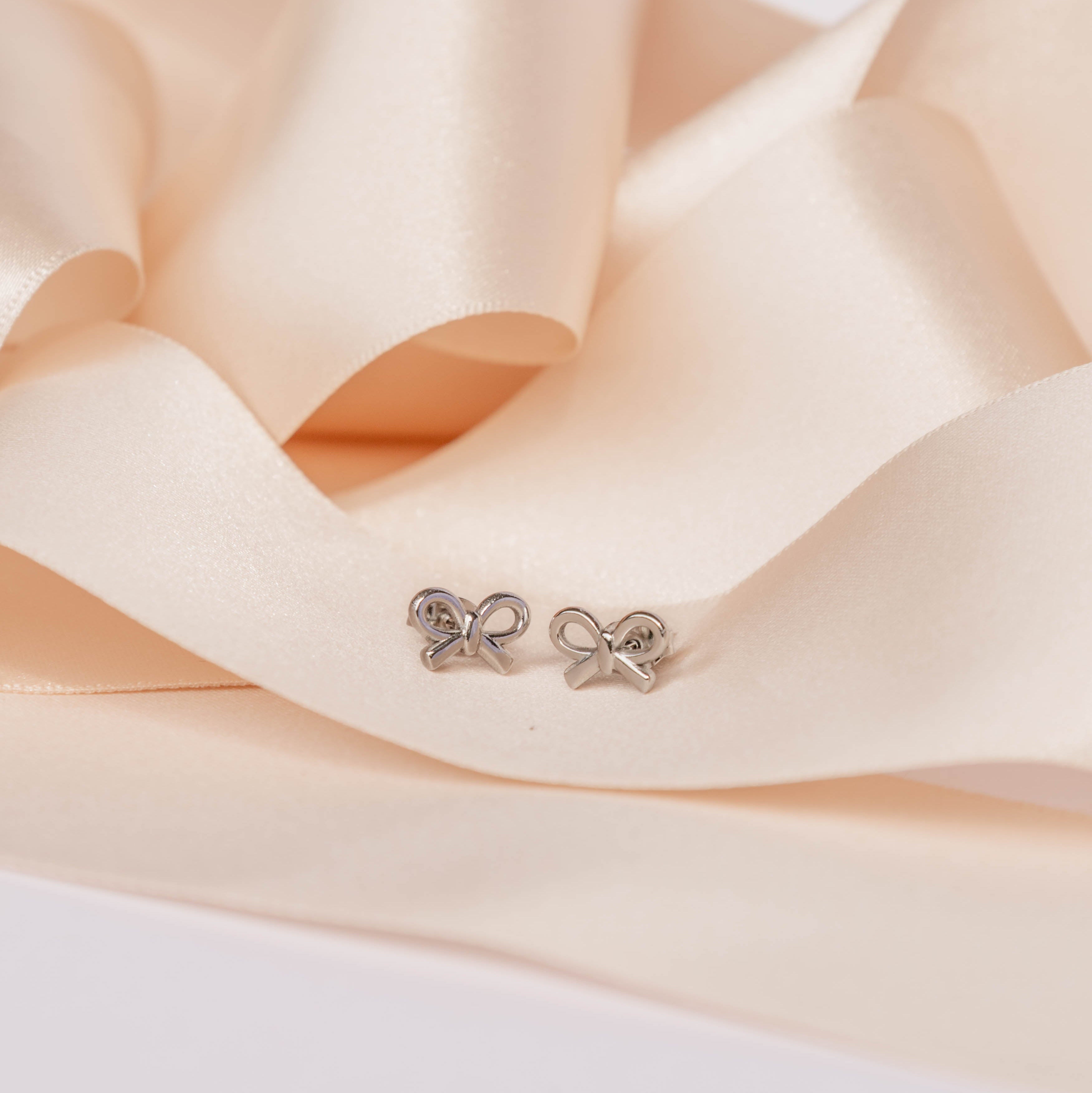 Silver bow-shaped earrings on a soft peach fabric background