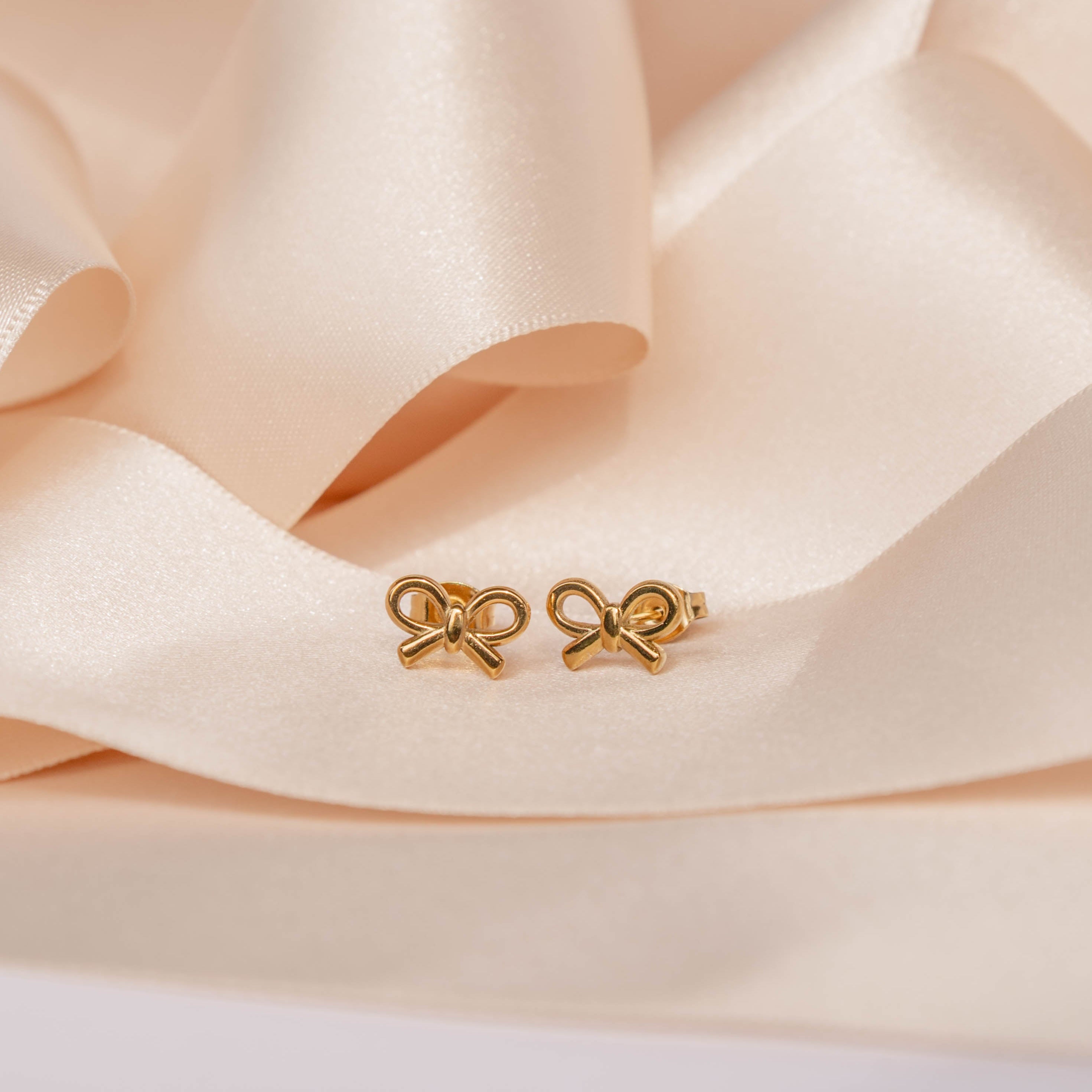 Gold bow-shaped earrings on a soft beige fabric background