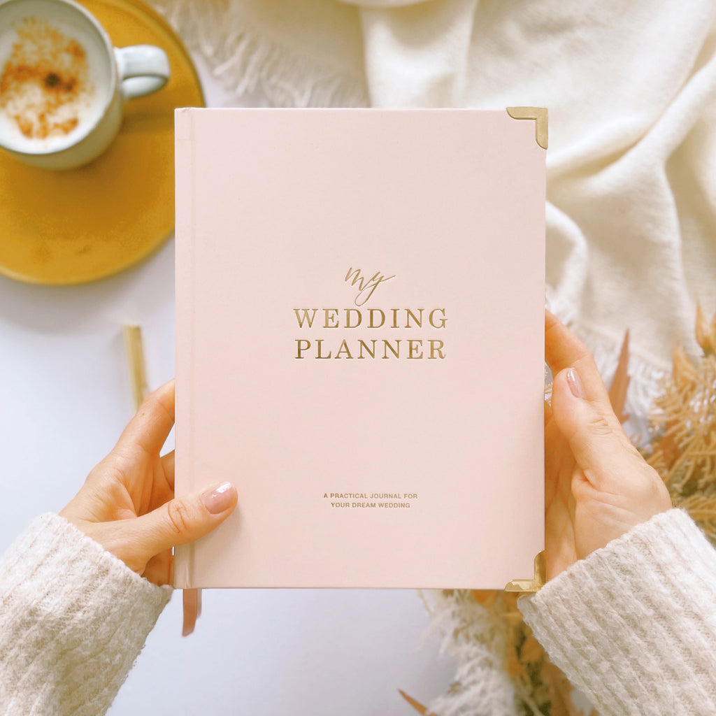 Pink wedding planner book held by hands with a cup of coffee in the background