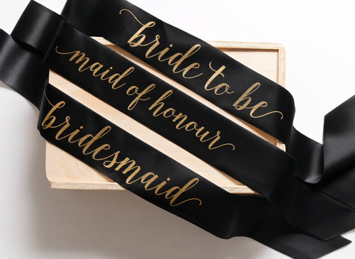 Black sash with gold text 'bride to be', 'maid of honour', and 'bridesmaid' on a white background.