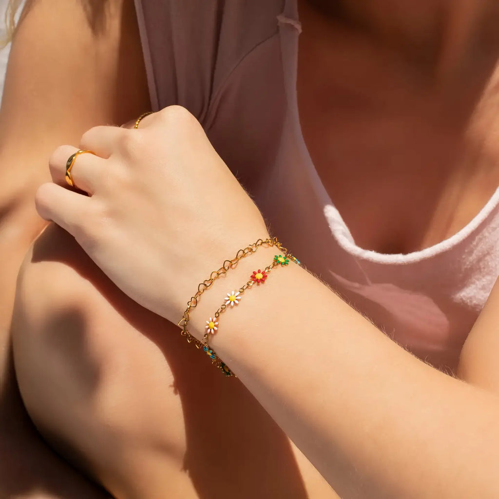 Close-up of a hand wearing a gold bracelet with colorful beads and a ring, against a blurred background.