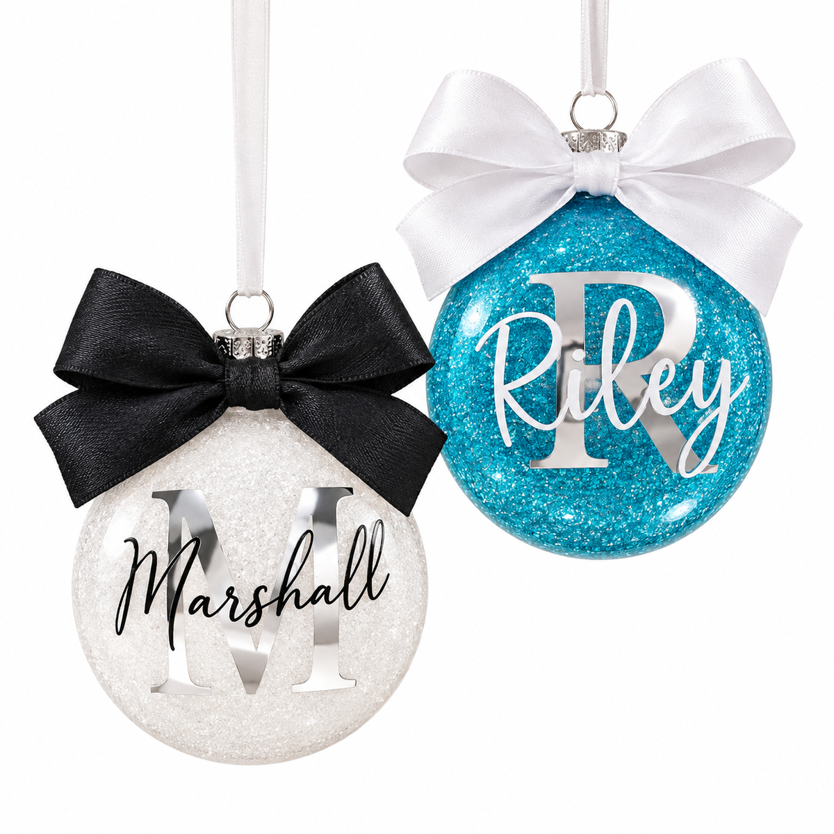 Two personalized round Christmas ornaments on white hanging ribbons. One ornament is white glitter with a black satin bow and silver lettering reading 'Marshall.