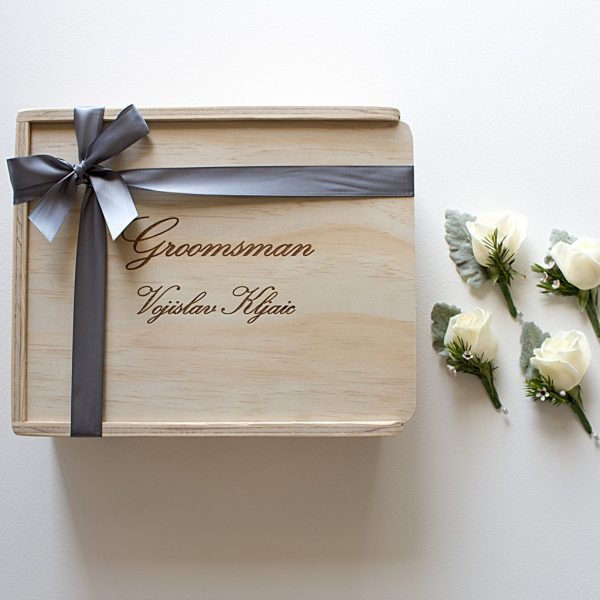 custom engraved groomsman wooden gift box with groomsman's name engraved on the lid, finished with bridal grey ribbon with white rose button holes beside it