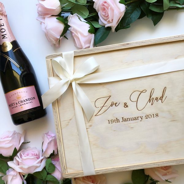 custom engraved wedding gift box with couple's name's and wedding date surrounded by champagne and pink roses. Box is finished with an ivory bow