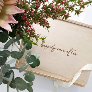 custom engraved gift box with floral arrangement in the foreground. Box is engraved with "happily ever after"