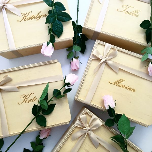 selection of wooden bridesmaid proposal boxes each custom engraved with names, including 'Kate' and 'Maria'. Decorated with champagne coloured ribbons and blush roses