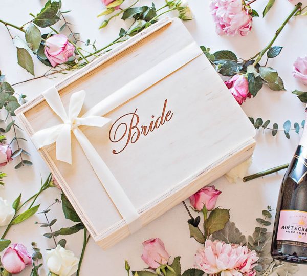wooden gift box with 'bride' engraved on the lid. Finished with an ivory ribbon and surrounded by pink roses and champagne