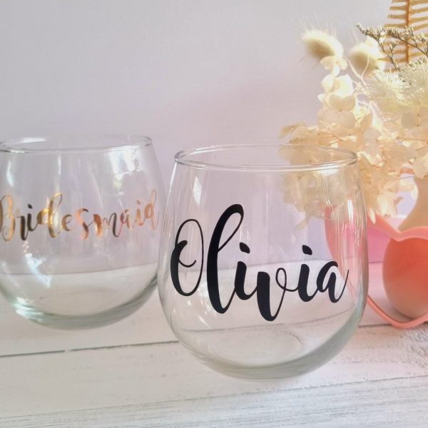 two personalised wine glasses one reading "olivia" in a black acrylic and one reading "bridesmaid" in a metallic gold acrylic