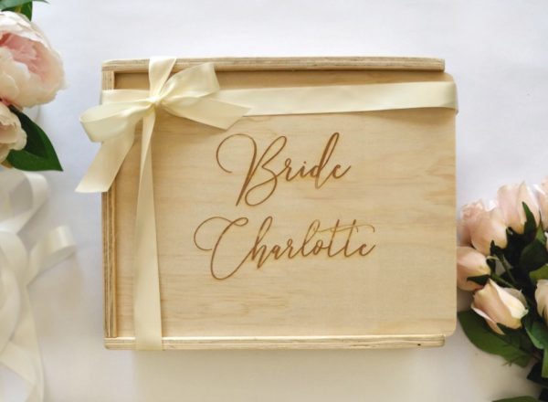 A wooden keepsake box engraved with "Bride Charlotte" finished with an ivory ribbon in frame decorated with blush roses