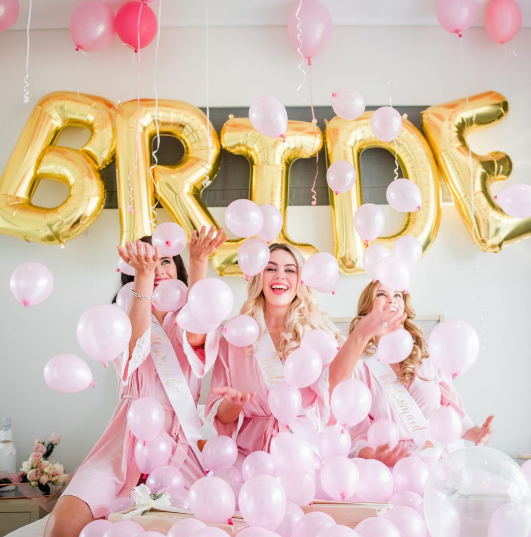 Bridesmaids in bridal party robes and bridesmaid sashes playing with balloons happily
