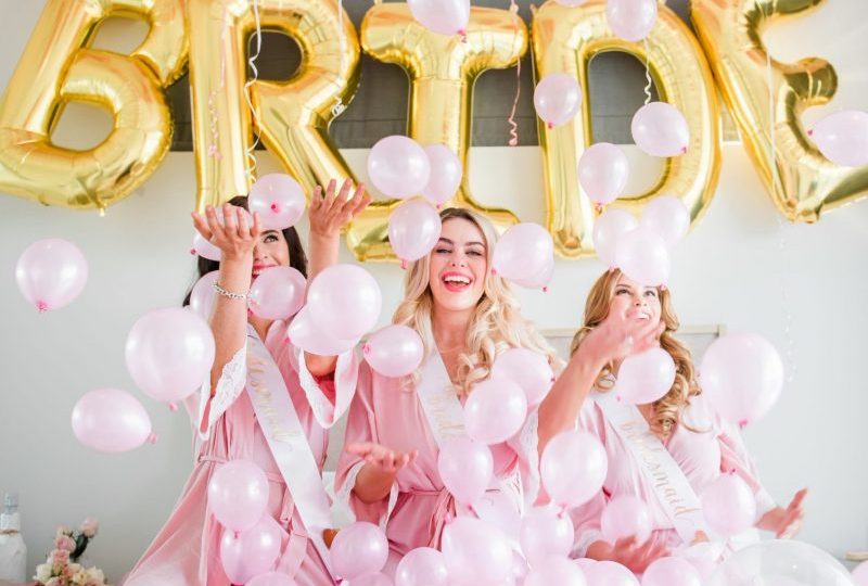 Bridesmaids in bridal party robes and bridesmaid sashes playing with balloons happily