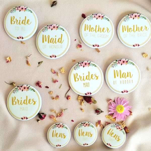 Hen's party badges for bachelorette party laid out on soft background surrounded by flowers