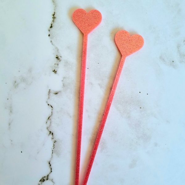 Closed heart stirrers in hot pink and shimmer pink on marble tile background