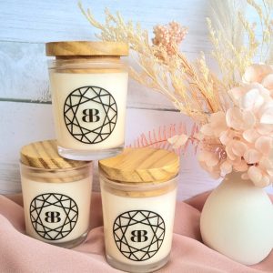 mini soy candles in clear jars with wooden lids, scented with champagne and strawberries or tropical orange in pyramid beside dried floral arrangement