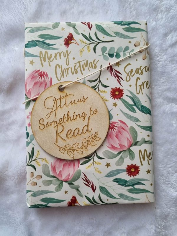 a custom engraved, personalised wooden gift tag that reads, "atticus somethin to read" tied to a brightly coloured, christmas themed gift