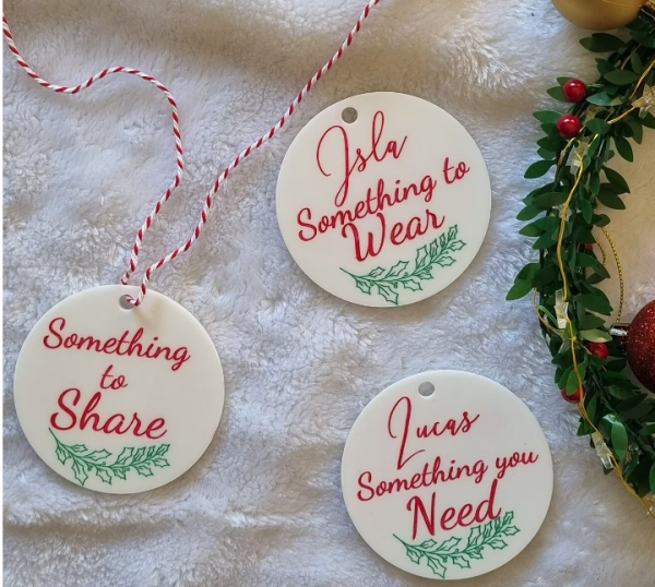 white acrylic gift tags that have wording, hand-painted in red with child's name and "something to wear, share and need" with a green, hand-pained misteltoe decoration