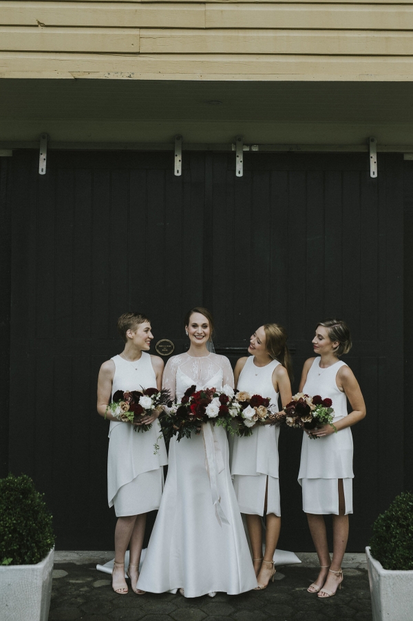 a bride posing with her bridesmaids, standing in front of a barn door