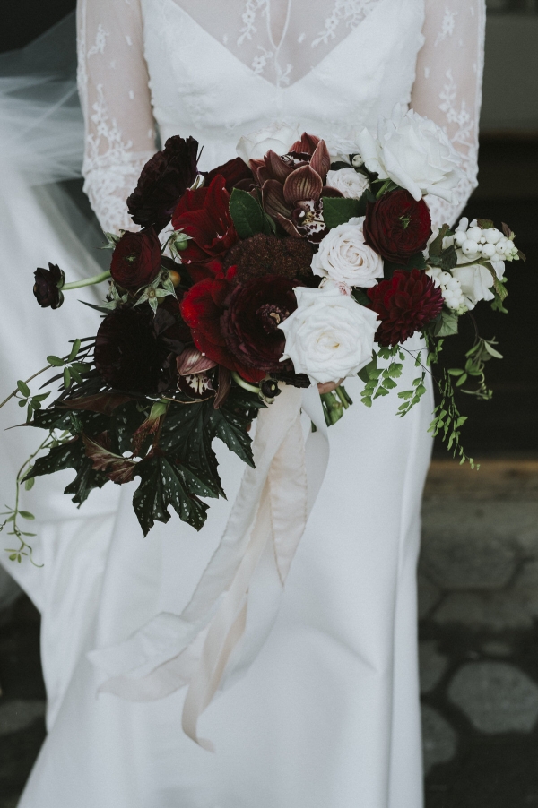a bridal bouquet of deep red flowers, greens and pops of white