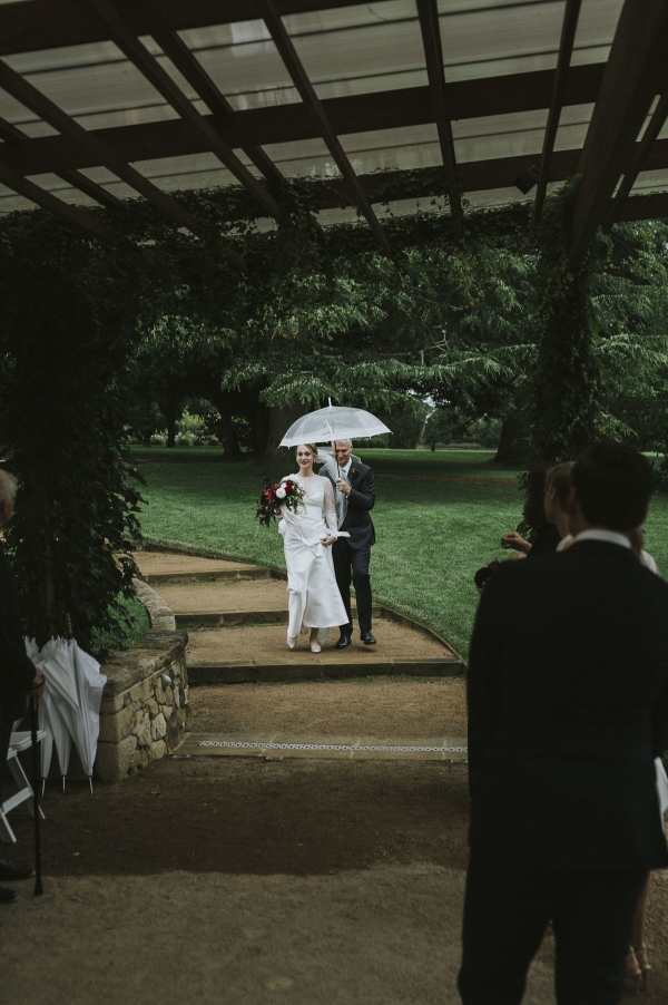 a bride walking down the aisle with her father in the rain
