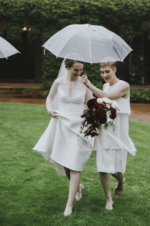 A bride being sheltered under a clear umbrella being held by her bridesmaid